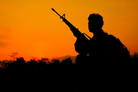 Silhouette shot of soldier holding gun with colorful sky and  mountain in backgroudの写真素材