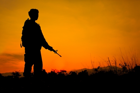 Silhouette shot of soldier holding gun with colorful sky and  mountain in backgroudの写真素材