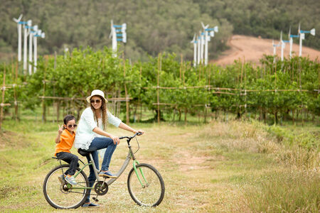 Woman and boy riding bicycle in farm with wind turbines in backgroundの写真素材