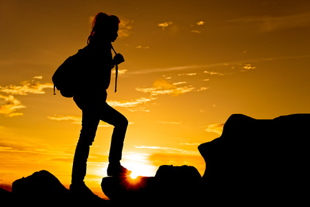 Woman walking on top of mountain at twilight with sun ray under her feetの写真素材