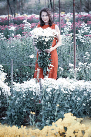 Beautiful Asian woman holding yellow flowers in hands with pride manner, flower garden owner satisfied with good quality flowers for sale.の写真素材