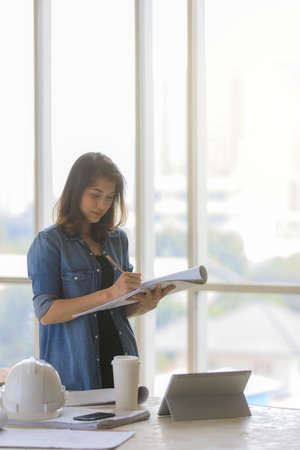 Asian female engineer in blue jeans shirt standing in constuction site with white helmetの写真素材