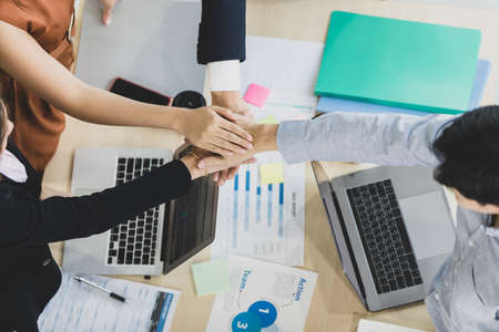 A Group of four businesspeople working around the desk and stack their hands together display the...