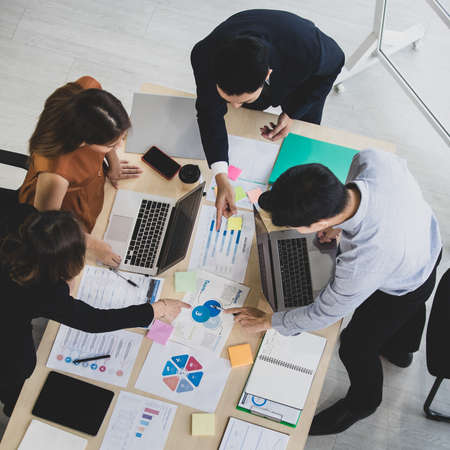 Group of four businesspeople working around desk and discuss for business plan graph and chart...