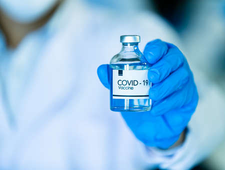 Hand in medical blue gloves holding a bottle of COVID-19 coronavirus vaccine.