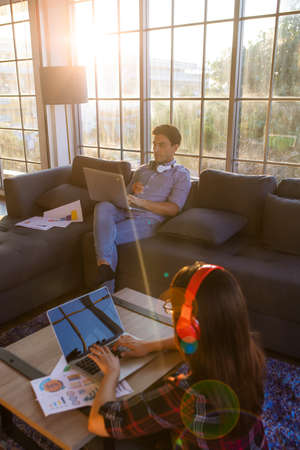 Caucasian man and Asian woman couple working at home in orange sunlight of evening twilight time...