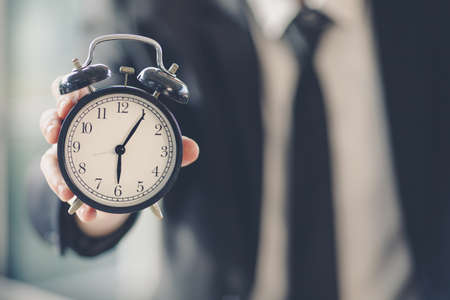Hand of businessman in black suit holding and show clock. Selective focus leave man blur in background. Idea for value of time in business work.の写真素材