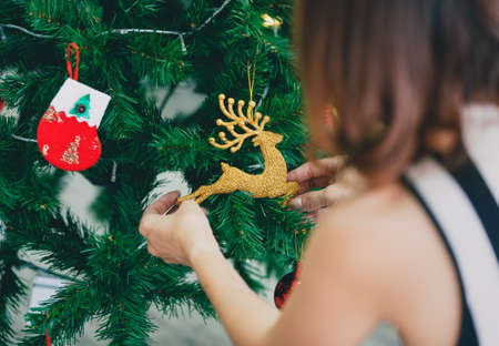 Back view of woman decorating and arranging Christmas tree at home and preparing for winter holidays.の写真素材