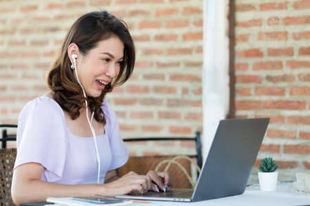 The beautiful middle-aged woman sitting in food shop and working with laptop notebook computer and...