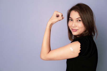 Portrait of vaccinated Asian woman showing plaster band aid on arm and show fist punch in winning...