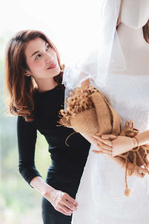 Gorgeous Asian woman prepares herself to be bride looking and review bridal gown in mannequin puppet...