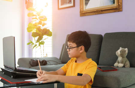 Young little boy wearing eyesglasses sitting near sofa in living room at home and do homework during...