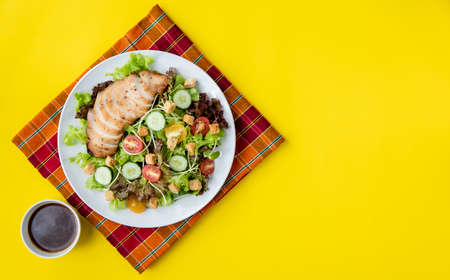 Top view shot of chicken salad  with several kinds of fresh vegetable in white plate on yellow...