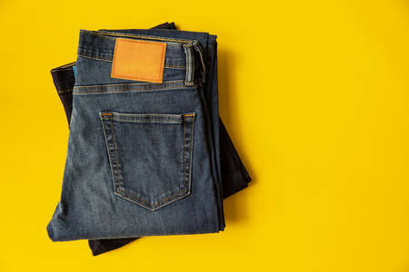 Stack of two folded new jeans trousers on yellow background with copy space.の写真素材