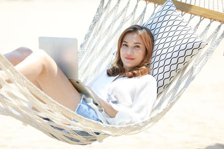 Beautiful Asian woman wearing sunglasses lay down on hammock nearby the seas with relaxing and happy...