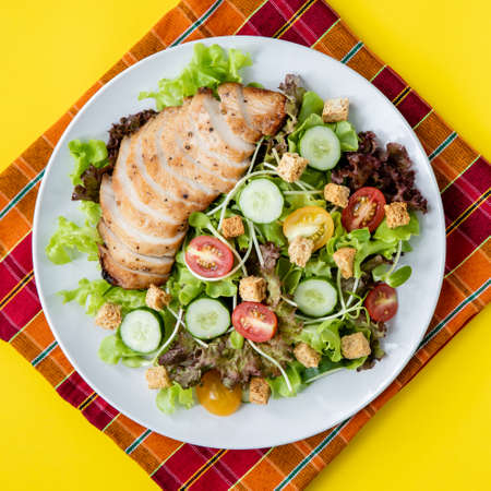 Top view shot of chicken salad  with several kinds of fresh vegetable in white plate on yellow...