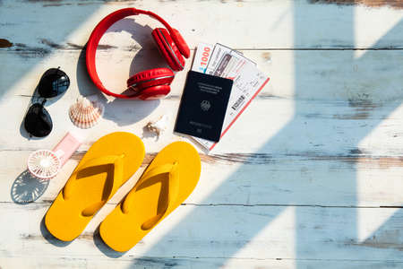 Set of travel accessories, bright yellow slippers with sunglasses, red headphone, and passport including airplane ticket, boarding pass voucher money on wood background with sunlight and copy space.の写真素材