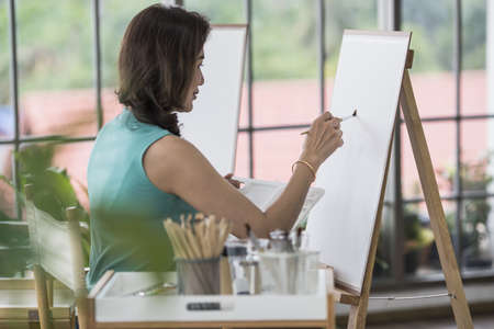 Beautiful lady Asian woman sitting and use a brush to pain picture in the room. Idea for hobby,...