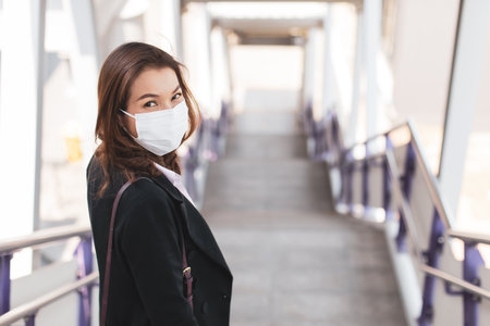 Beautiful Asian woman in a black suit wearing medical hygiene protective mask walking on stair in city to work at office. Idea for health care and prevent from risk of coronavirus epidemic outbreak.の写真素材