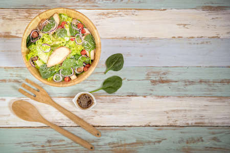 Chicken and mix vegetables salad in wood bowl with wooden folk on wooden plate colorful background with copy space and sauce. Idea for health care and diet food with copy space.の写真素材