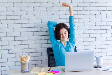 Young and cute half race Thai German woman sitting at working desk and stretch herself with hands over the head for relaxing and calm to get rid of lazy during long work in house. Work at home idea.の写真素材
