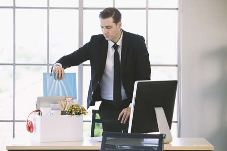 Young Caucasian businessman put document file holder  and belongings into paper box prepare to go back home in the end day after get fired from his job. Concept for out of work in modern office.の写真素材