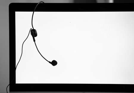 Headphone headset hanging on edge of blank computer screen monitor. The idea for call center work and take a break during working hours.の写真素材