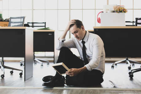 Young caucasian businessman in suit tired sitting with feeling sad, looking to family photo in frame use hand to hold his head in office at end of job day. Idea for unemployed person, work crisis.の写真素材