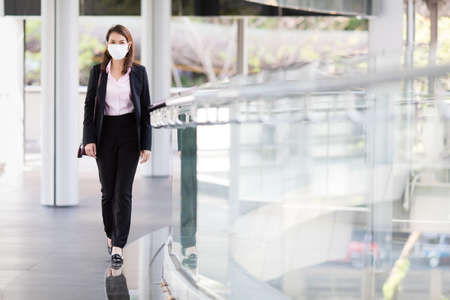 Beautiful cute Asian businesswoman wearing protective surgical hygiene mask on face in the situation of coronavirus outbreak, walking to office in city. Idea for preventing, protect health from virus.の写真素材
