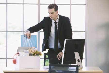 Young Caucasian businessman put document file holder  and belongings into paper box prepare to go back home in the end day after get fired from his job. Concept for out of work in modern office.の写真素材