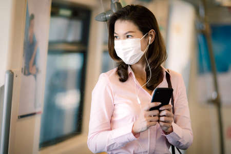 Beautiful cute smiley Asian businesswoman wearing protective surgical hygiene mask on face prevent...