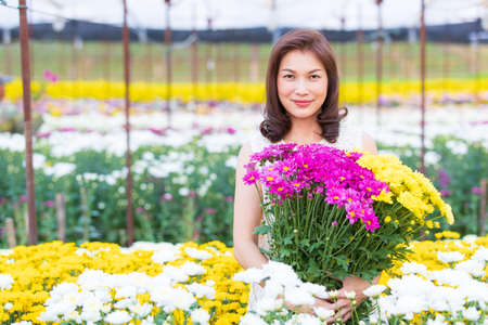 Beautiful Asian woman holding yellow flowers in hands with pride manner, flower garden owner satisfied with good quality flowers for sale.の写真素材