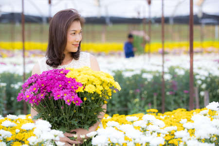 Beautiful Asian woman holding yellow flowers in hands with pride manner, flower garden owner satisfied with good quality flowers for sale.の写真素材