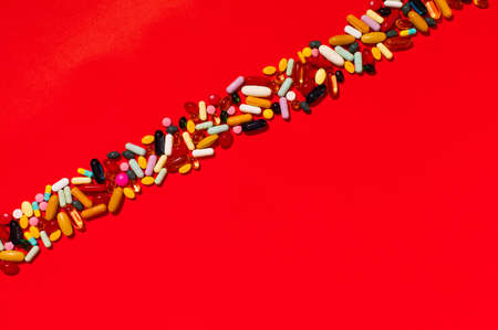 Group of assorted pharmaceutical medicine pills, colorful tablets and capsules with strong light and shadows on red  paper background. Wide panorama ratio crop.の写真素材