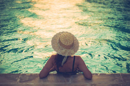Woman wear big hat standing on water beside swimming pool with orange sunlight. Prccess in vintage...
