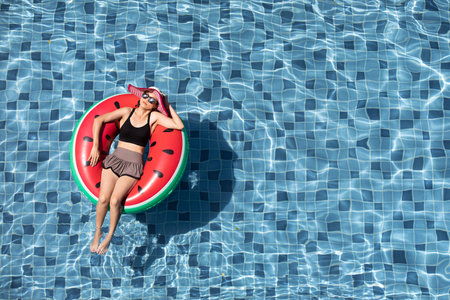 Top view shot woman wear sunglasses laying on balloon in blue water swimming pool with copy space, concept for luxury and happy lifestyle.の写真素材