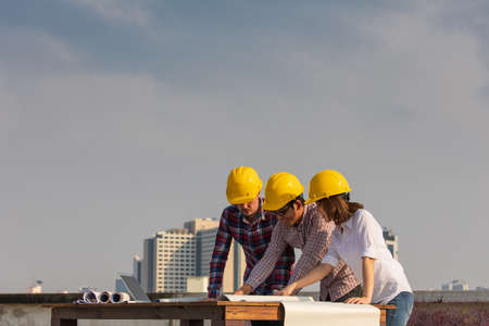 Diverse group of three engineer, caucacian and Asian, in construction site looking at blueprint plan and brainstorm during working on rooftop of building with copyspace on top.の写真素材