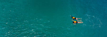 Couple catch each other hands and swim, skin diving to sea reef in clear water near island in Thai sea. Concept for sharing good time together and lifestyle of modern lovers. Panorama crop.の写真素材