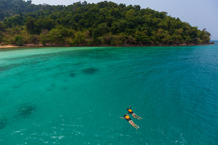 Couple catch each other hands and swim, skin diving to sea reef in clear water near island in Thai sea. Concept for sharing good time together and lifestyle of modern loversの写真素材