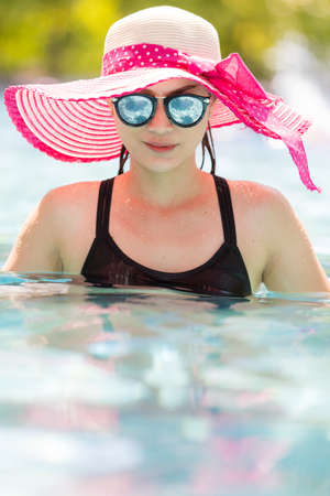Portrait of 40s adult Asian woman wear sunglasses and put on big hat standing in pool and looking to water with reflection in lens.の写真素材