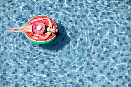 Top view shot woman wear sunglasses laying on balloon in blue water swimming pool with copy space, concept for luxury and happy lifestyle.の写真素材