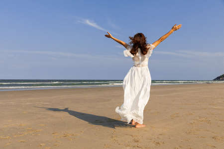 Woman wear white dress standing alone on sand beach and looking to see with blue sky in background with happiness manner.の写真素材