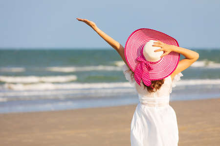 Woman wear white dress and red hat  standing alone on sand beach and looking to see with blue sky in background with happiness manner.の写真素材