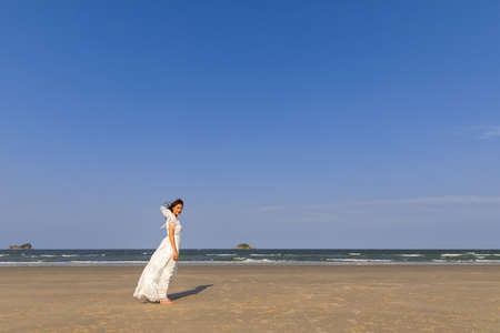 Woman wear white dress standing alone on sand beach and looking to see with blue sky in background with happiness manner.の写真素材