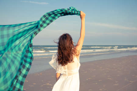 Woman in white dress holding waver cloth playing in strong wind on beach with happiness and freedom manner.の写真素材