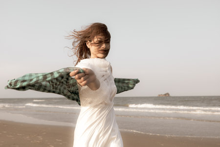 Woman in white dress holding waver cloth playing in strong wind on beach with blow hair on face in happiness and freedom manner.の写真素材
