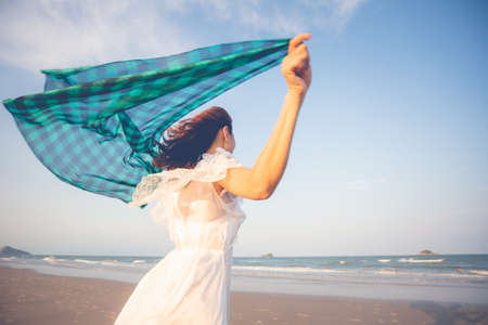 Woman in white dress holding waver cloth playing in strong wind on beach with happiness and freedom manner.の写真素材