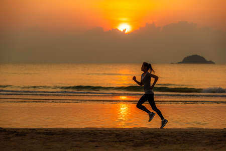 Woman running on beach at sunrise with water and wave in background.の写真素材