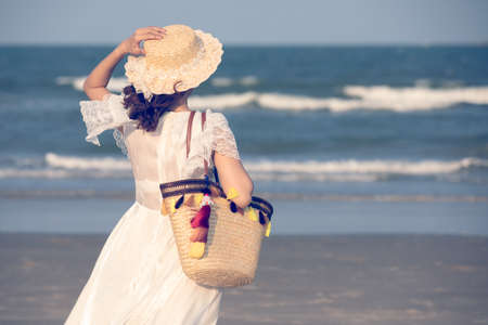 Woman carry big handcraft bag wearing beautiful hat standing and looking to sea with wave and background.の写真素材