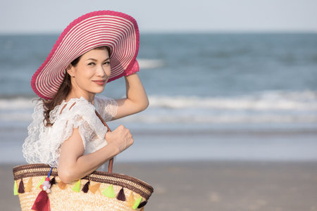 Woman carry big handcraft bag wearing beautiful hat standing and looking to camra with wave and background. Process in retro film style.の写真素材